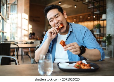 Happy  Asian man eating BBQ chicken wings in restaurant. - Shutterstock ID 2091026020