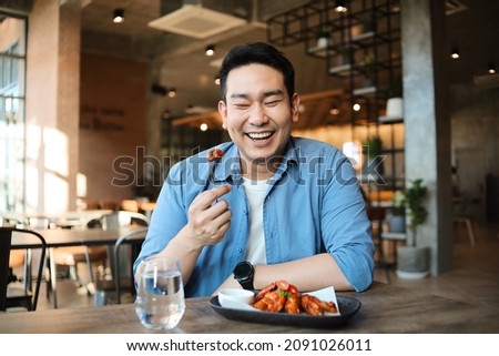 Happy  Asian man eating BBQ chicken wings in restaurant.
