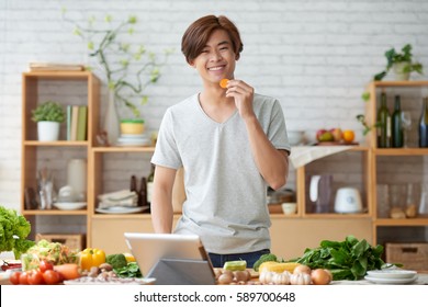 Happy Asian Man Eating Slice Of Carrot When Cooking