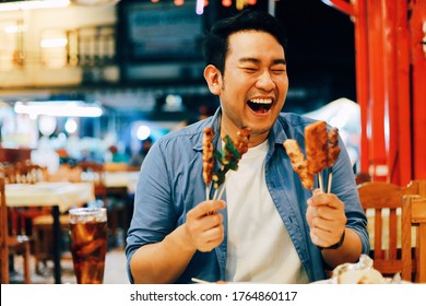 Happy Asian man eating street food at local market.