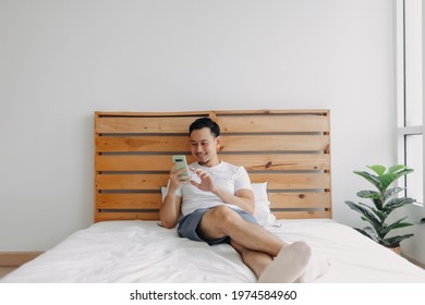 Happy Asian man feels relax with smartphone on his bed on day time.