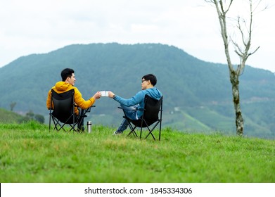 Happy Asian man friends sitting on the mountain with talking and drinking coffee together in autumn. Smiling two handsome guy couple relax and enjoy with outdoor lifestyle camping on holiday vacation - Powered by Shutterstock