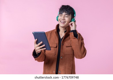 Happy Asian a man handsome young in headphones is listening to music using a tablet to the side eyes looking at camera in love isolated on pink blank copy space studio background. - Powered by Shutterstock