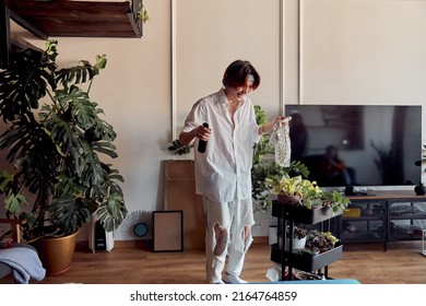 Happy Asian Man In Headphones Watering Plants At Home