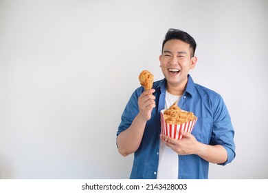 Happy Asian man holding fried chicken bucket standing over white background with copy space. - Shutterstock ID 2143428003