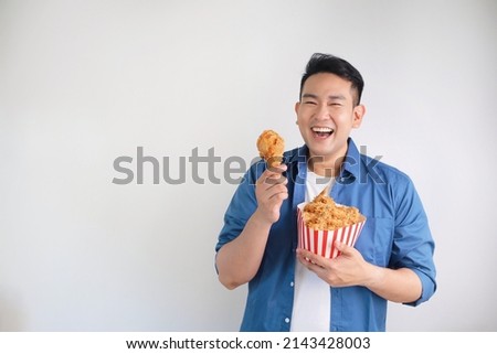 Happy Asian man holding fried chicken bucket standing over white background with copy space.