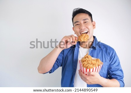 Happy Asian man holding fried chicken bucket standing over white background with copy space.