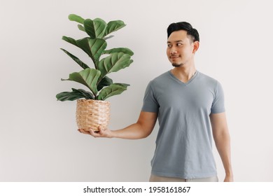 Happy Asian Man Holding A House Plant Isolated On White Background.