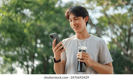 Happy asian man holding mobile phone and bottle of water at public park, Male using smartphone, checking mobile fitness application. - Powered by Shutterstock