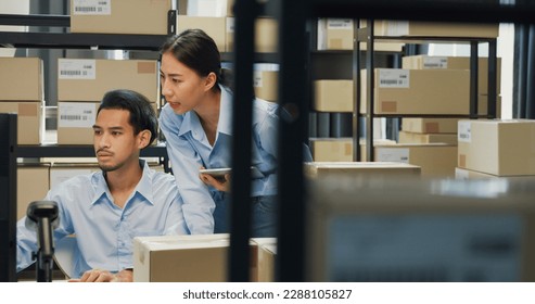 Happy Asian man and lady partner wear formal shirt sit in front of desk computer and barcode machine scanner discuss stock detail customer online data delivery at warehouse. Startup business concept. - Powered by Shutterstock