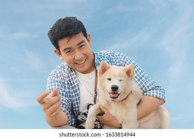 Happy Asian Man With Lovely Dog Over Blue Sky Background.