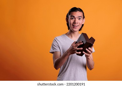 Happy Asian Man Opening Gift Box, Unpacking Birthday Surprise. Smiling Young Person Unboxing Present, Holding Small Cardboard Delivery Package With Excited Facial Expression