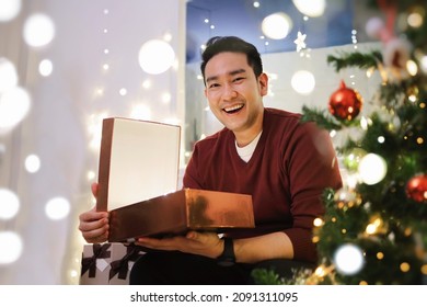 Happy Asian Man In Red Sweater Unboxing Christmas Gift At Home.