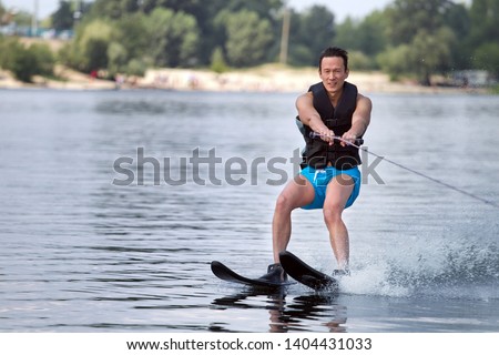 Happy asian man riding water skis on lake in summer