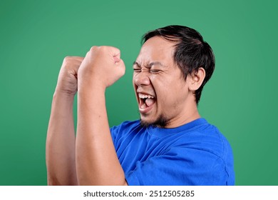 Happy Asian Man Screaming And Clenched Fist Showing Victory Gesture Over Green Screen - Powered by Shutterstock