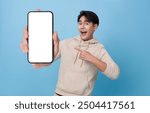 Happy Asian man showing and pointing finger to smartphone mockup of blank screen isolated on blue background.