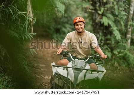 happy asian man smiling to camera while riding atv through the track at amusement park