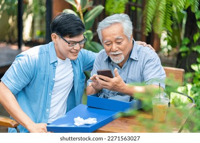 Happy Asian man teaching elderly father using mobile phone application during having lunch together at restaurant on summer vacation. Family relationship senior people mental health care concept. - Powered by Shutterstock