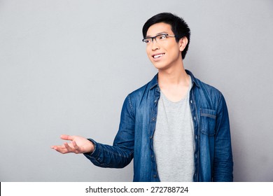 Happy Asian Man Telling Something And Gesturing With Hand Over Gray Background. Looking Away