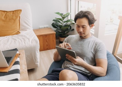 Happy Asian man use tablet for work on bean bag in the living room of the house. - Powered by Shutterstock