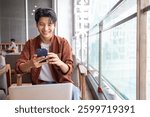 Happy Asian man using mobile phone and working with computer laptop while sitting in coffee shop