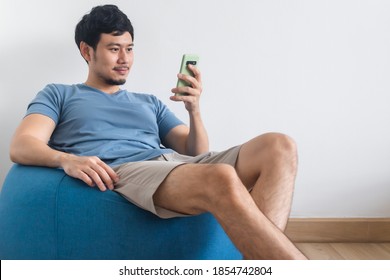 Happy Asian Man Is Using Smartphone While Sit And Relax On The Beans Bag.