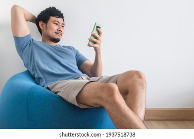 Happy Asian Man Is Using Smartphone While Sit And Relax On The Beans Bag.