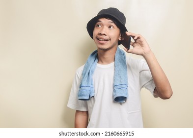 Happy Asian Man Wearing Bright White T-shirt With Black Hat With Blue Towel Playing Phone On Isolated Background