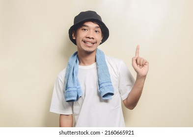 Happy Asian Man Wearing Bright White T-shirt With Black Hat Carrying Blue Towel On Isolated Background