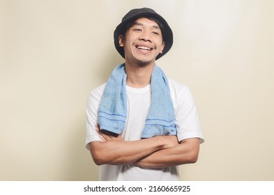 Happy Asian Man Wearing Bright White T-shirt With Black Hat Carrying Blue Towel On Isolated Background