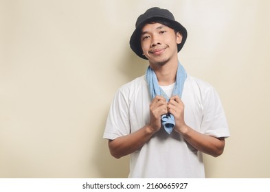 Happy Asian Man Wearing Bright White T-shirt With Black Hat Carrying Blue Towel On Isolated Background