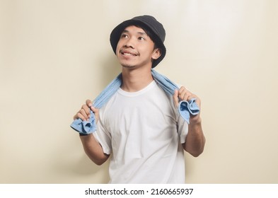 Happy Asian Man Wearing Bright White T-shirt With Black Hat Carrying Blue Towel On Isolated Background