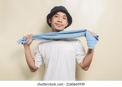 Happy Asian Man Wearing Bright White T-shirt With Black Hat And Carrying Towel On Isolated Background