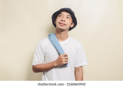 Happy Asian Man Wearing Bright White T-shirt With Black Hat And Carrying Towel On Isolated Background