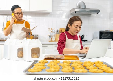 Happy Asian man and woman bakery shop owner working on laptop computer and preparing customer order selling online delivery in kitchen. Small business food and drink occupation entrepreneur concept. - Powered by Shutterstock