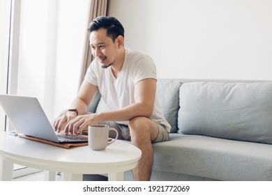 Happy Asian Man Is Working On His Laptop In The Living Room.