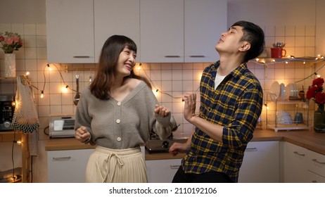 Happy Asian Married Couple Enjoying Dancing Together By Moving Body Toward Each Other On A Valentine Night Date In The Kitchen At Home