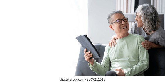 Happy Asian mature couple using a digital tablet in living room, spending time and bonding with each other. - Powered by Shutterstock