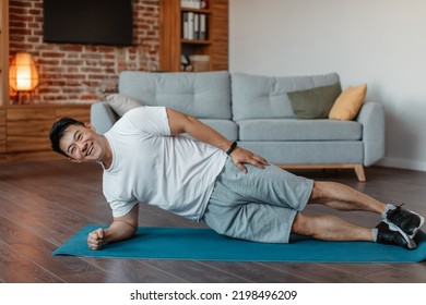 Happy Asian Mature Man In Sportswear Doing Side Plank On Floor Mat In Living Room Interior, Copy Space. Sport At Home, Workout, Fitness And Exercises, Active Lifestyle