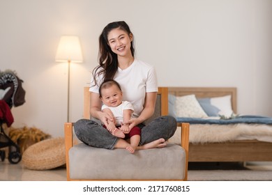 Happy Asian Mom Playing And Spending Time With Her Newborn Baby And Looking At Camera Together At Home. Adorable Baby Boy Smile Laughing With Mother In Warmth Place Relax And Comfortable.good Moment