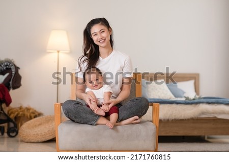Happy asian mom playing and spending time with her newborn baby and looking at camera together at home. Adorable baby boy smile laughing with mother in warmth place relax and comfortable.good moment
