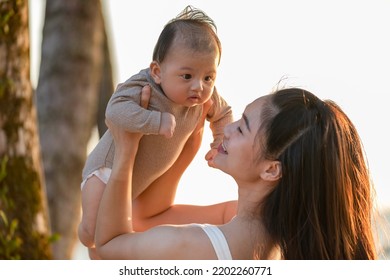 Happy Asian Mom Raise Baby Up Playing And Laughing Together With Sunset Light.Mother Lift Up Her Baby Or Daughter To The Sky With Love And Good Moment.Outdoor Family Activity.Mom And Baby Concept