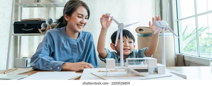 Happy Asian Mom Teaching Little Boy For The Future With Windmill Model On Workplace At Home. Asian Kid With Mother At Home Together.