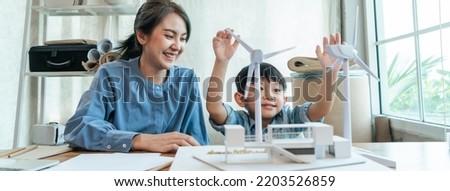 Happy Asian mom teaching little boy for the future with windmill model on workplace at home. Asian kid with mother at home together.