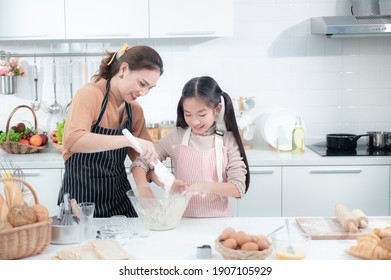 Happy Asian Mother Is Caring And Teaching Adorable Daughter Helping Knead The Dough To Make A Bakery And Cooking In The Modern Kitchen For Enjoy Eating And A Family Party.