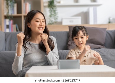 Happy Asian Mother And Daughter Sing A Song And Dancing Together Watching Music Video Apps In Smartphone.Cheerful Mom And Kid Recording Video Clip And Sharing On Social Media Streaming App Having Fun