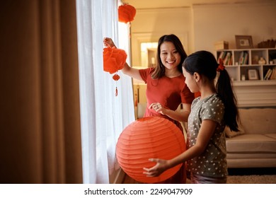 Happy Asian mother enjoying while hanging red lanterns with her daughter for Chinese New Year celebration at home. - Powered by Shutterstock