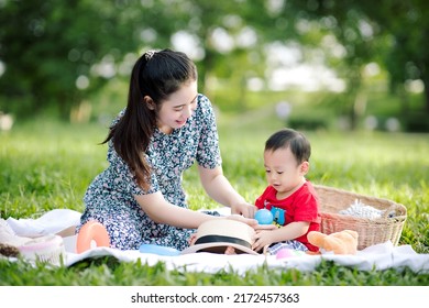 Happy Asian mother and little baby son playing while picnic in the park on a holiday, the family having fun and spending time together, Happy family concept.
