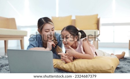 Happy asian mother and little daughter sharing laptop enjoying leisure together while lying on floor in living room. Mother and daughter watching movie on laptop in weekend. Single mother concept