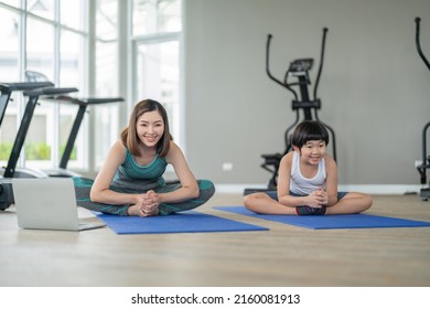 Happy Asian Mother And Son Wearing Sportswear Practices Yoga Online With Laptop Together In Small Gym Sports Club